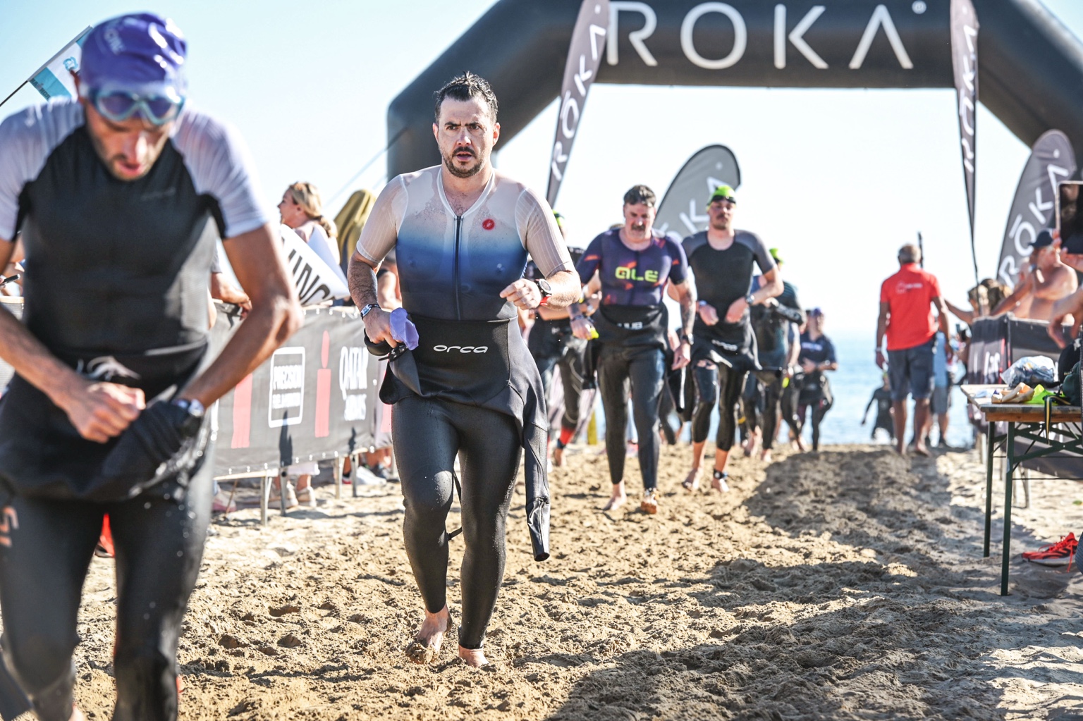 Damian wychodzi z wody na plażę w stroju triathlonowym i opuszczonej piance.